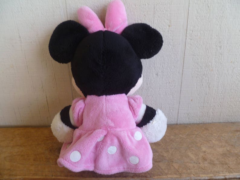 Puede incluir: Un juguete de peluche rosa y negro de un rat&oacute;n de dibujos animados que lleva un vestido rosa con lunares blancos. El rat&oacute;n tiene un lazo rosa en la cabeza.