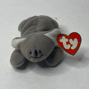 May include: Gray plush koala beanie baby toy with a white Ty tag attached. The tag has the word "ty" in red letters.