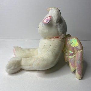 May include: White plush angel bear with iridescent wings and a halo. The bear has a pink nose and a pink tag that says "Ty" with a heart.