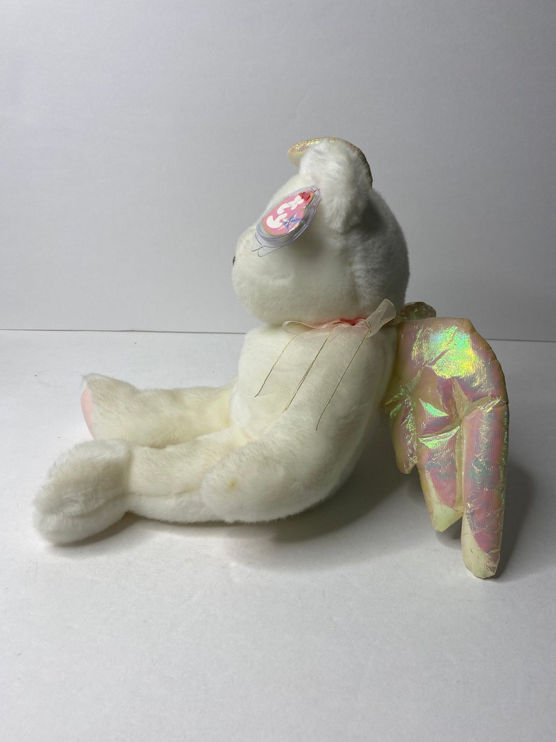 May include: White plush angel bear with iridescent wings and a halo. The bear has a pink nose and a pink tag that says "Ty" with a heart.