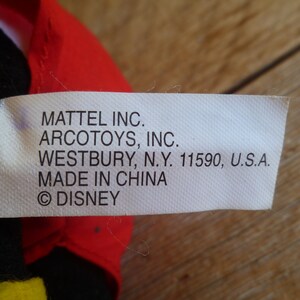 Może przedstawiać: Biała metka z czarnym tekstem, kt&oacute;ry brzmi: "MATTEL INC. ARCOTOYS, INC. WESTBURY, N.Y. 11590, U.S.A. MADE IN CHINA &copy;DISNEY"