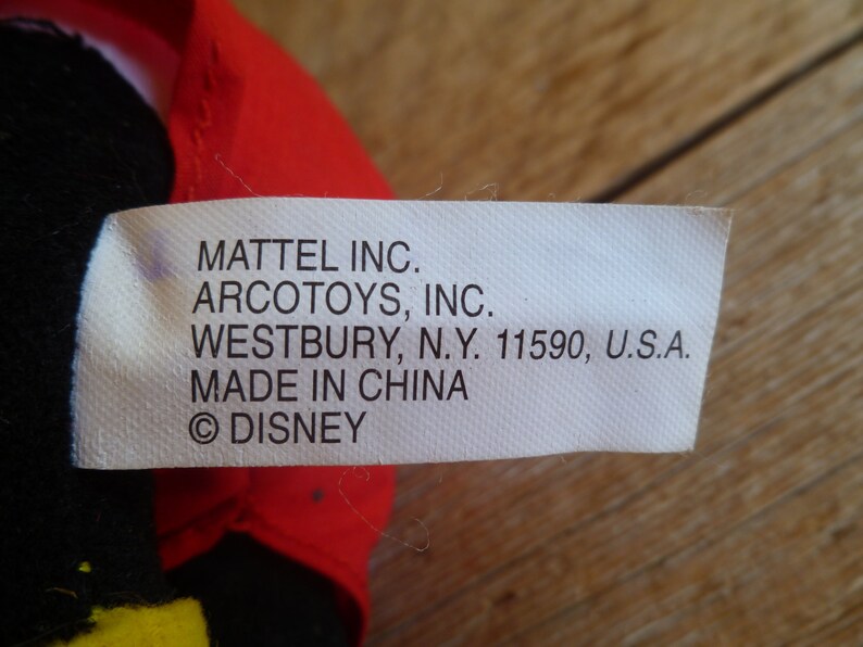 Może przedstawiać: Biała metka z czarnym tekstem, kt&oacute;ry brzmi: "MATTEL INC. ARCOTOYS, INC. WESTBURY, N.Y. 11590, U.S.A. MADE IN CHINA &copy;DISNEY"