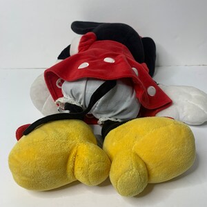Pu&ograve; includere: Un giocattolo di peluche rosso e nero di Minnie Mouse. Il giocattolo &egrave; sdraiato sulla schiena con le braccia e le gambe distese. Il giocattolo indossa un vestito rosso con pois bianchi e un fiocco nero.