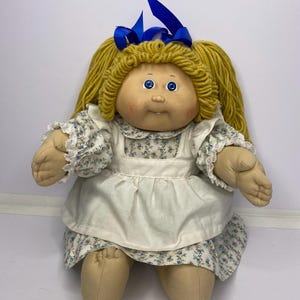 以下が含まれることがあります： 黒い持ち手と「But First, Coffee」の太字の黒い文字が入った白いセラミックマグ。マグカップはニュートラルな背景に置かれ、シンプルなデザインを際立たせています。