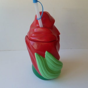 May include: Red plastic cup shaped like a rose with green leaves. The cup has a straw sticking out of the top.