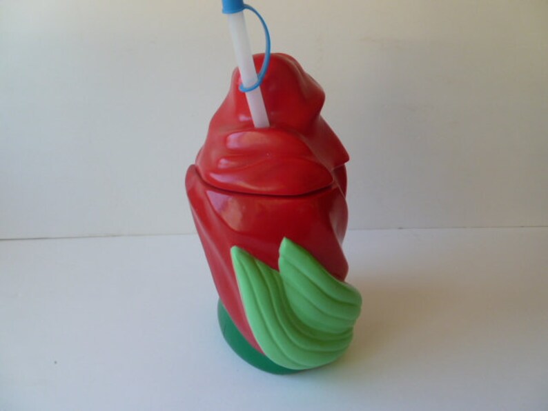 May include: Red plastic cup shaped like a rose with green leaves. The cup has a straw sticking out of the top.