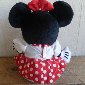 Op de afbeelding: Een pluche speelgoed van een cartoonmuis die een rood-wit geblokt jurkje draagt met een rode strik op haar hoofd.