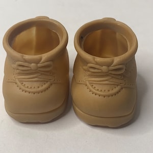 Op de afbeelding: Een paar bruin-beige miniatuurschoenen. De schoenen hebben een klassiek ontwerp met een strikdetail en decoratieve perforaties. Ze zijn gemaakt van een stevig materiaal en zijn ontworpen voor een kleine pop of figuur.
