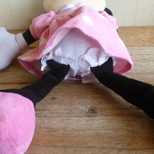 May include: A pink and white polka dot dress with white lace trim and black legs. The dress is worn by a plush toy.