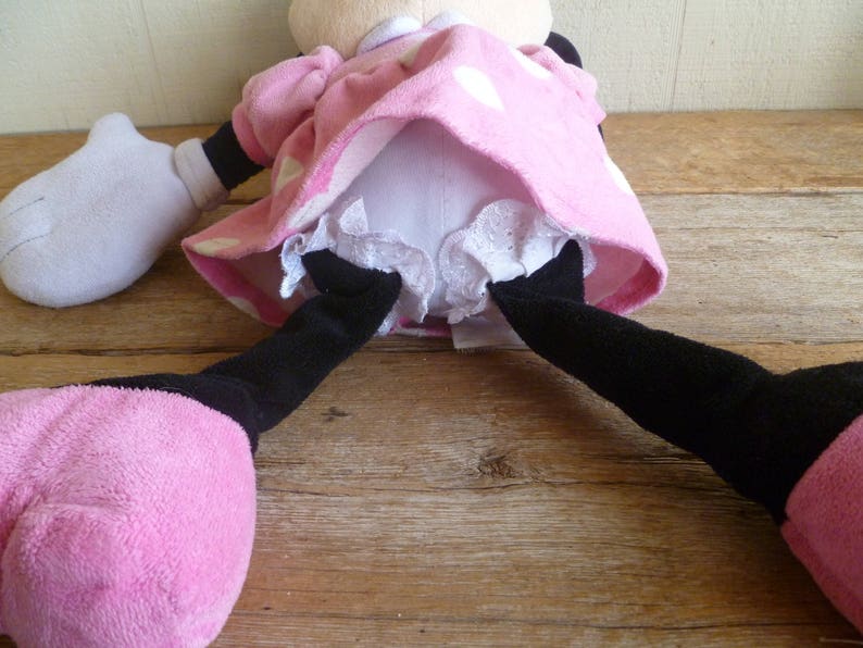 May include: A pink and white polka dot dress with white lace trim and black legs. The dress is worn by a plush toy.
