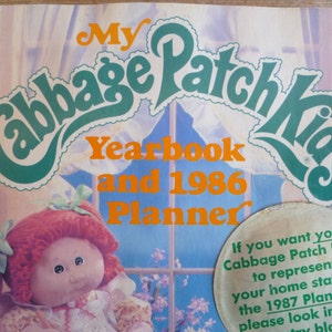 May include: A vintage Cabbage Patch Kids yearbook and planner from 1986. The cover features a red-haired Cabbage Patch Kid doll with a pink and white dress. The title "My Cabbage Patch Kids Yearbook and 1986 Planner" is in green and orange lettering.