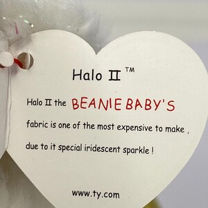 K&ouml;nnte beinhalten: Ein wei&szlig;es herzf&ouml;rmiges Etikett mit dem Text "Halo II" und "BEANIE BABY'S". Auf dem Etikett steht, dass der Stoff aufgrund seines schillernden Funkelns teuer ist. Die Website www.ty.com ist ebenfalls sichtbar.