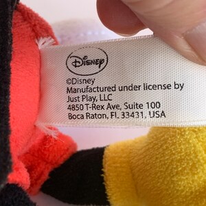 Op de afbeelding: Een close-up van een Disney-productlabel. Het label is wit met het Disney-logo en de tekst "&copy;Disney Vervaardigd onder licentie door Just Play, LLC 4850 T-Rex Ave, Suite 100 Boca Raton, Fl. 33431, USA."