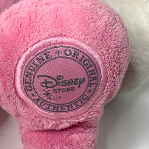 May include: Pink plush toy with a round, gray tag that says "Genuine + Original Disney Store Authentic".