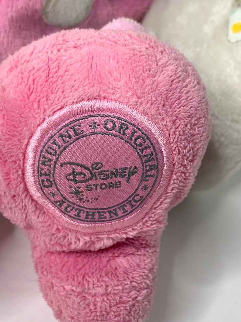 May include: Pink plush toy with a round, gray tag that says "Genuine + Original Disney Store Authentic".