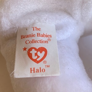 May include: White Beanie Baby plush toy with a red tag that reads "The Beanie Babies Collection&reg;" with a star and the Ty logo. The tag also reads "Halo" with a registered trademark symbol.
