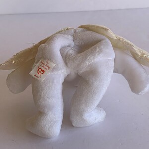 May include: White plush angel beanie baby with gold wings and a red heart tag that reads "The Beanie Babies Collection" and "Halo".