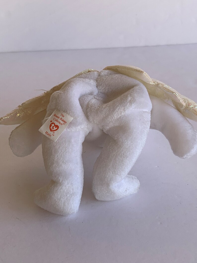 May include: White plush angel beanie baby with gold wings and a red heart tag that reads "The Beanie Babies Collection" and "Halo".