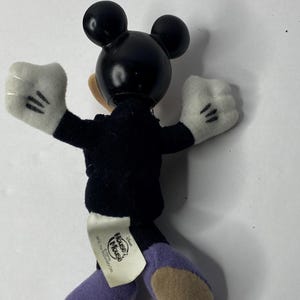 May include: A black and white plush Mickey Mouse toy wearing a black suit and purple shoes. The toy has a tag on its back that says "Disney's House of Mouse" and "&copy; Disney.  All rights reserved."