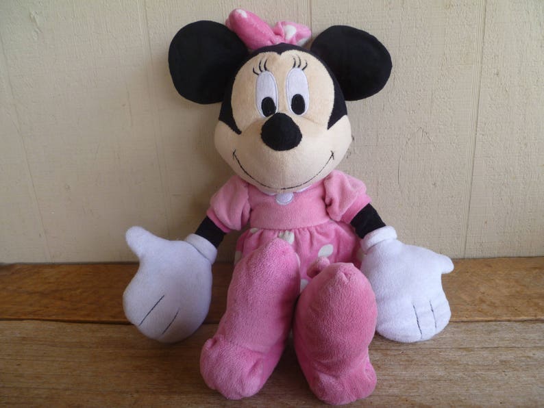 May include: A pink and white polka dot dress with a pink bow on top of the head. The plush toy has black ears and a black nose.