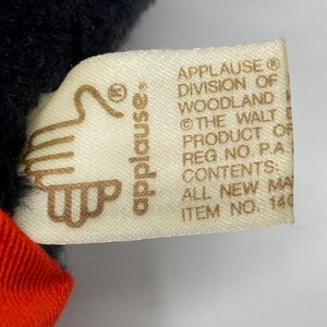 May include: A white tag with brown text that reads "APPLAUSE&reg; DIVISION OF WOODLAND &copy; THE WALT DISNEY PRODUCT OF REG. NO. P.A. CONTENTS: ALL NEW MATERIAL ITEM NO. 140". The tag is attached to a black plush toy.