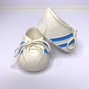 May include: A pair of white baby shoes with blue stripes and laces. The shoes have a classic sneaker design, perfect for a newborn. The shoes are made of a soft material.