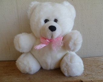Peut inclure: Ours en peluche blanc avec un nœud rose. L'ours a des yeux noirs et un nez noir.