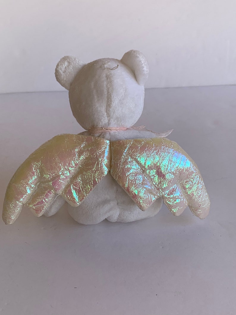 May include: White plush teddy bear with iridescent wings. The bear is sitting with its back to the camera. The wings are spread out behind the bear.
