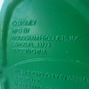 May include: Green plastic container with the text "DISNEY MFG BY MONOGRAM PRODUCTS, INC. LARGO, FL. 33773 MADE IN CHINA WASH THOROUGHLY IN WARM WATER BEFORE USE NOT DISHWASHER SAFE" printed on the bottom.