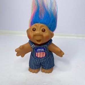 May include: A vintage troll doll with a smiling expression and colorful hair. The doll wears denim overalls with a "Union Pacific" patch. The hair is a mix of blue, pink, yellow, and orange.
