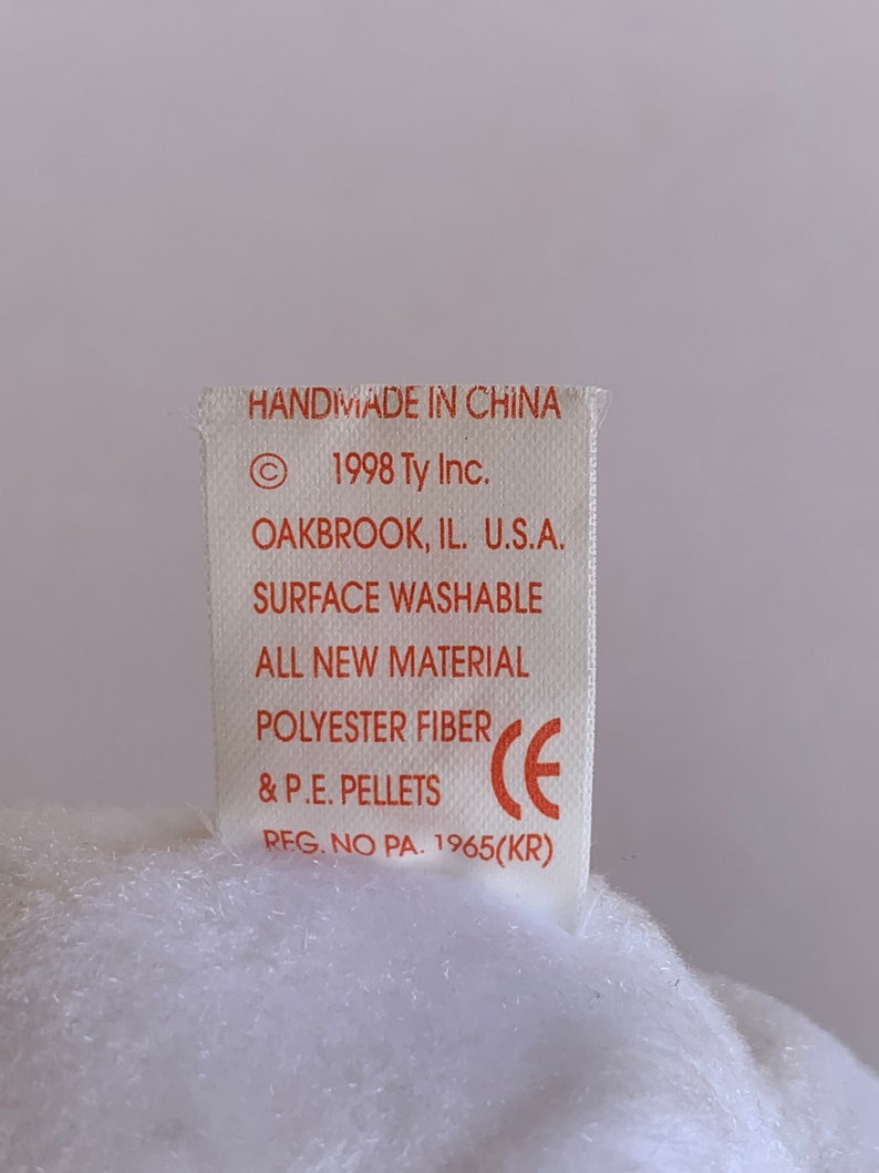 May include: A white tag with red text that reads "Handmade in China", "1998 Ty Inc.", "Oakbrook, IL. U.S.A.", "Surface Washable", "All New Material", "Polyester Fiber", "& P.E. Pellets", "Reg. No PA. 1965(KR)" and a CE mark.