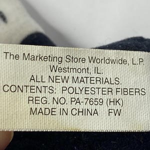 May include: White tag with black text on a black fabric background. The tag reads "The Marketing Store Worldwide, L.P. Westmont, IL. ALL NEW MATERIALS. CONTENTS: POLYESTER FIBERS REG. NO. PA-7659 (HK) MADE IN CHINA FW"