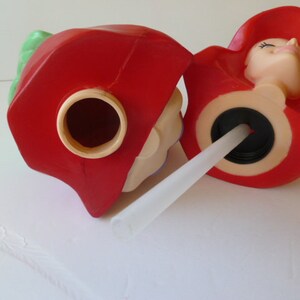 May include: Two red plastic figures with a straw inserted into one of the figures. The figures have a hole in the top and a hole in the bottom. The figures are shaped like a person with a hat.