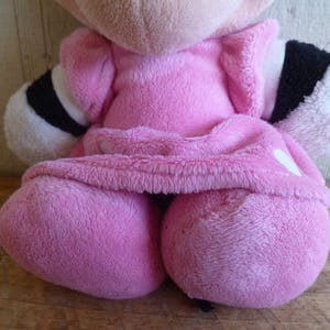 Puede incluir: Un juguete de peluche rosa con detalles en blanco y negro. El juguete lleva un vestido rosa y tiene un coraz&oacute;n blanco en el pecho.