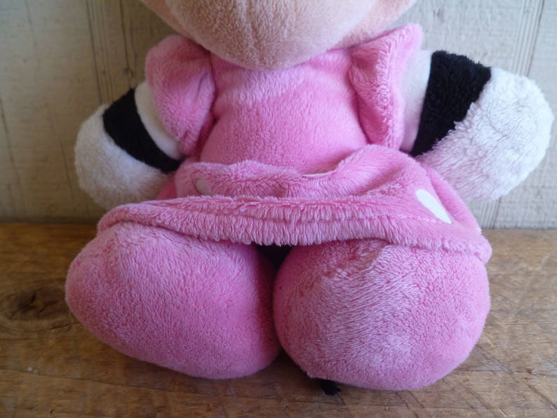 Puede incluir: Un juguete de peluche rosa con detalles en blanco y negro. El juguete lleva un vestido rosa y tiene un coraz&oacute;n blanco en el pecho.