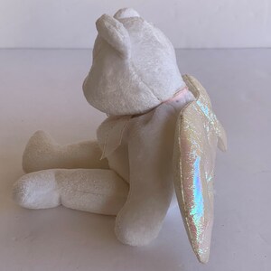 May include: White plush angel bear with iridescent wings. The bear is sitting with its head tilted back and its wings are spread out behind it.