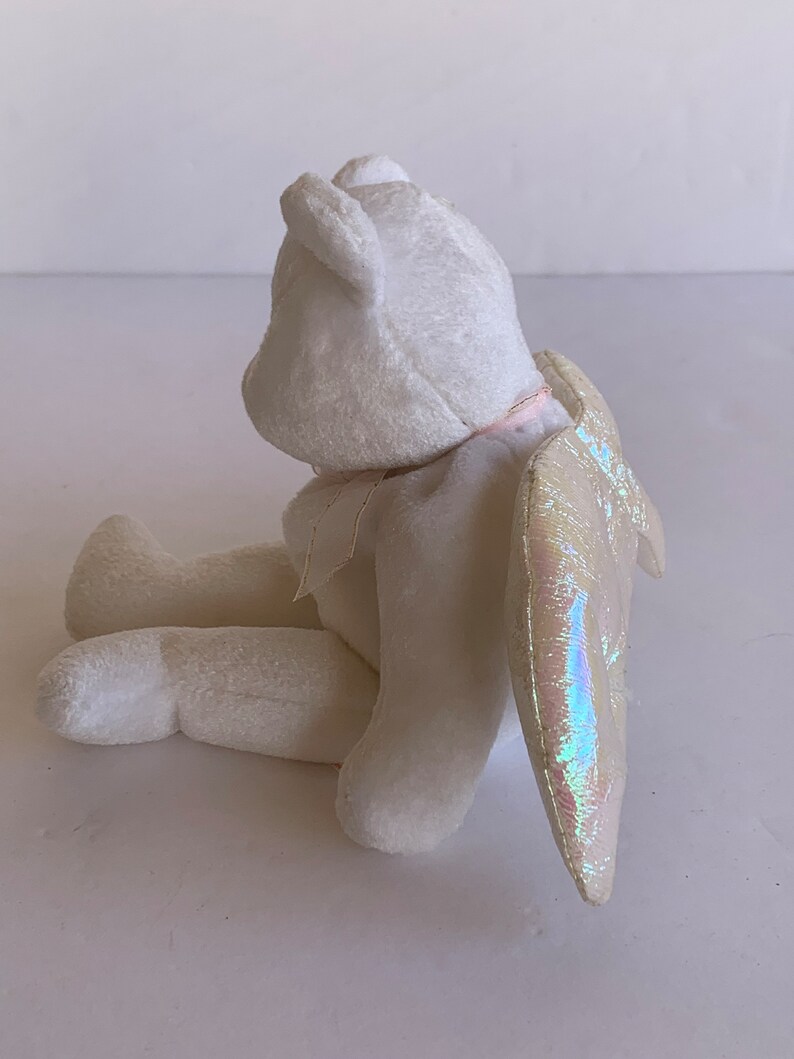 May include: White plush angel bear with iridescent wings. The bear is sitting with its head tilted back and its wings are spread out behind it.