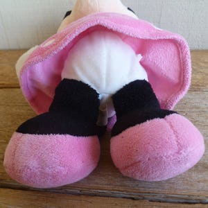 Puede incluir: Juguete de peluche rosa con piernas negras y vientre blanco. El juguete lleva una falda rosa con lunares blancos.