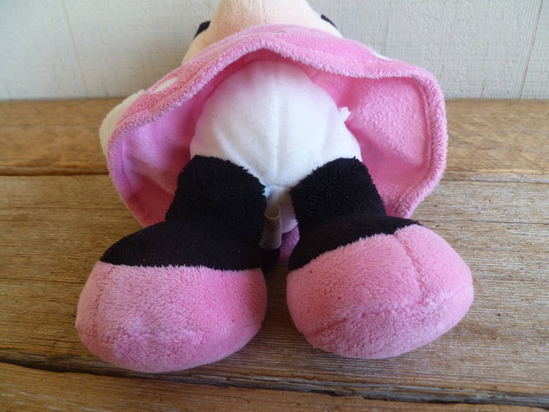 Puede incluir: Juguete de peluche rosa con piernas negras y vientre blanco. El juguete lleva una falda rosa con lunares blancos.