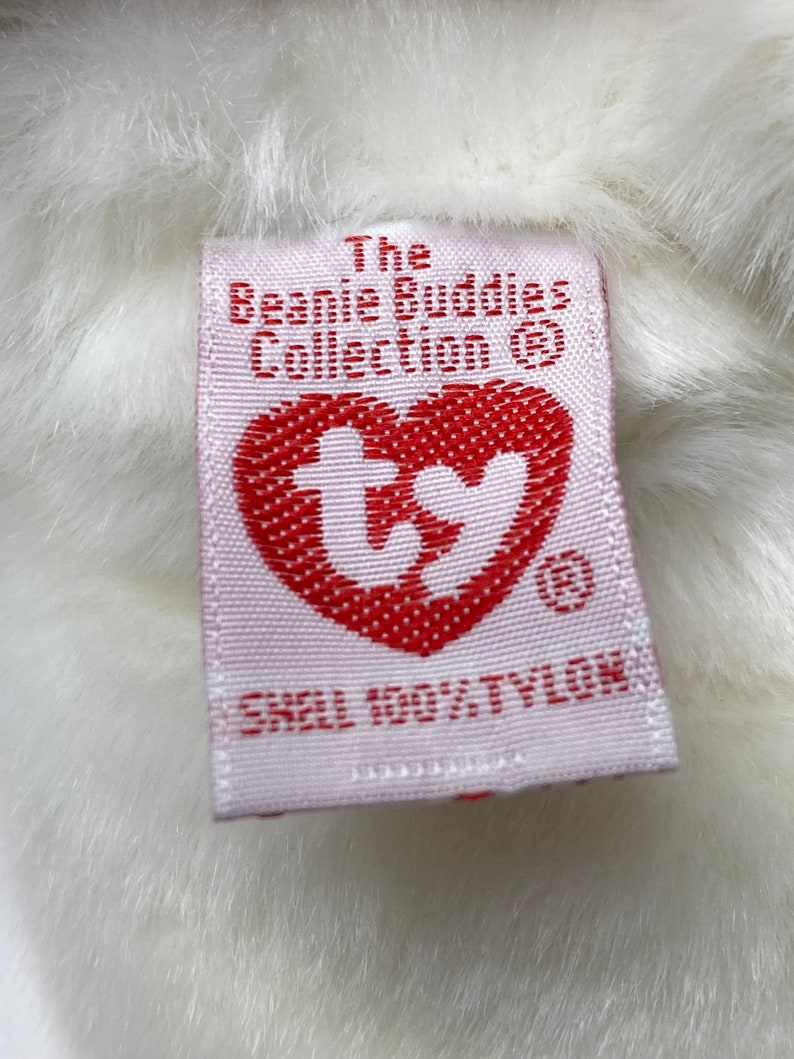 May include: White plush toy with a pink tag that reads "The Beanie Buddies Collection&reg;" and a red heart with the Ty logo. The tag also says "Shell 100% Tylok."