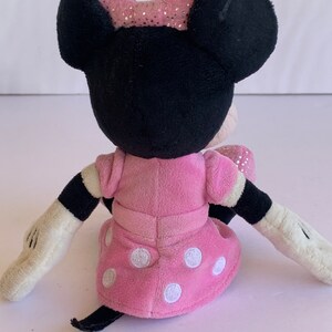 May include: A pink plush Minnie Mouse toy with white polka dots on her dress. She has black ears and a pink bow with glitter on top.
