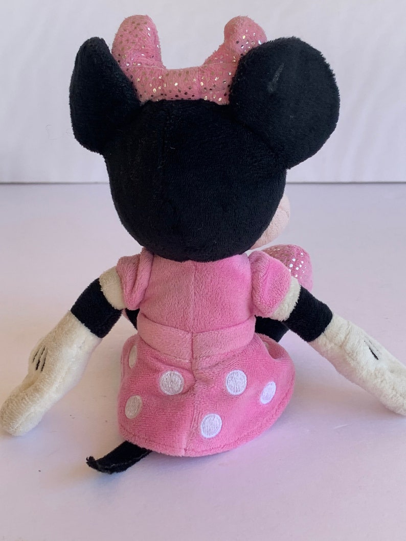May include: A pink plush Minnie Mouse toy with white polka dots on her dress. She has black ears and a pink bow with glitter on top.