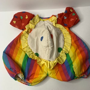 May include: A rainbow striped and red fabric clown costume with yellow ruffles and white polka dots. The costume has a white fabric circle in the center with blue and green polka dots.