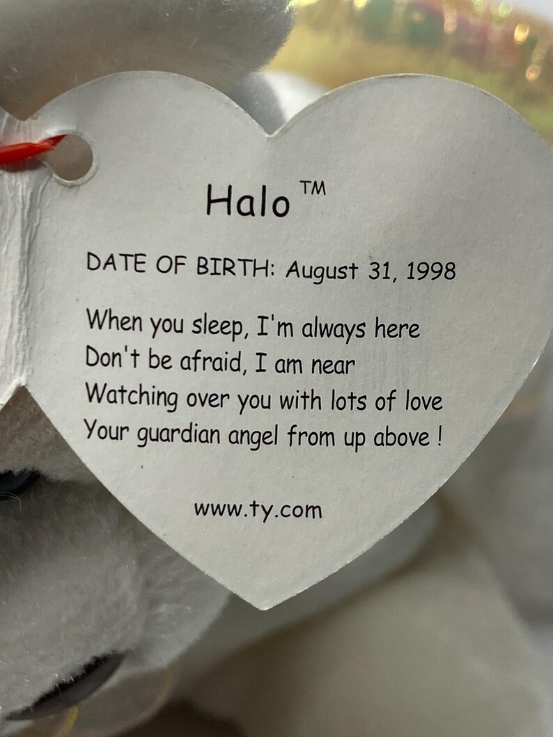 以下が含まれることがあります： 白いぬいぐるみで、ハート型のタグが付いています。タグには「Halo TM DATE OF BIRTH: August 31, 1998 When you sleep, I'm always here Don't be afraid, I am near Watching over you with lots of love Your guardian angel from up above! www.ty.com」と書いてあります。