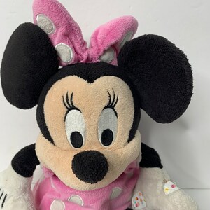 May include: A pink and black plush Minnie Mouse toy wearing a pink polka dot dress and a pink bow with white polka dots.