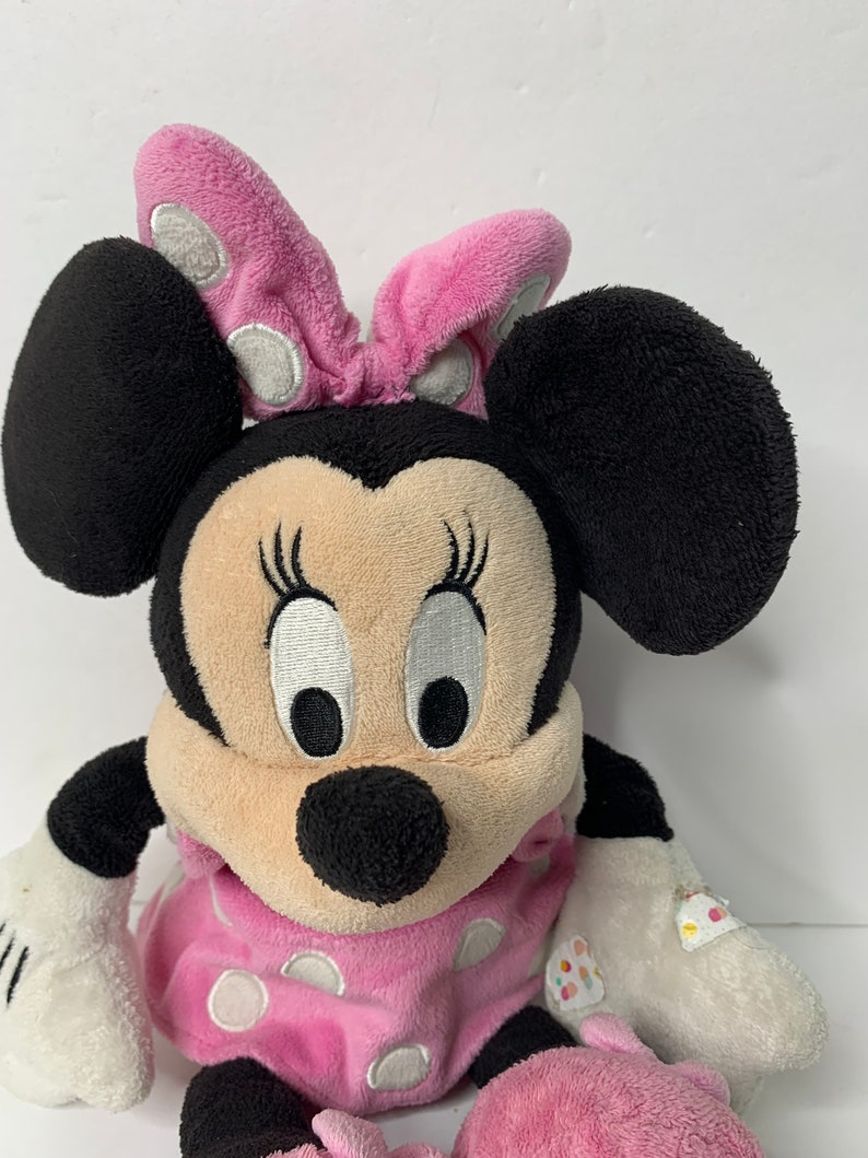 May include: A pink and black plush Minnie Mouse toy wearing a pink polka dot dress and a pink bow with white polka dots.