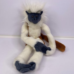 May include: A plush toy of a cotton-top tamarin monkey with long white fur on its head, white fur on its arms and legs, and dark gray fur on its face, hands, and feet. The monkey has a brown tail and brown fur on its lower back and torso.