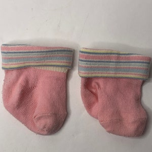 May include: A pair of pink baby socks with a striped cuff in shades of blue, yellow, and pink.