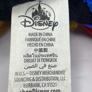 May include: A white tag with the Disney logo and text in multiple languages, including "MADE IN CHINA" and "shopDisney.com". The tag also includes the address of Disney Merchandise Sourcing & Distribution, LLC in Burbank, CA.