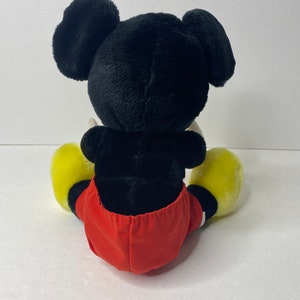 May include: A black and red plush Mickey Mouse toy sitting down with yellow shoes.